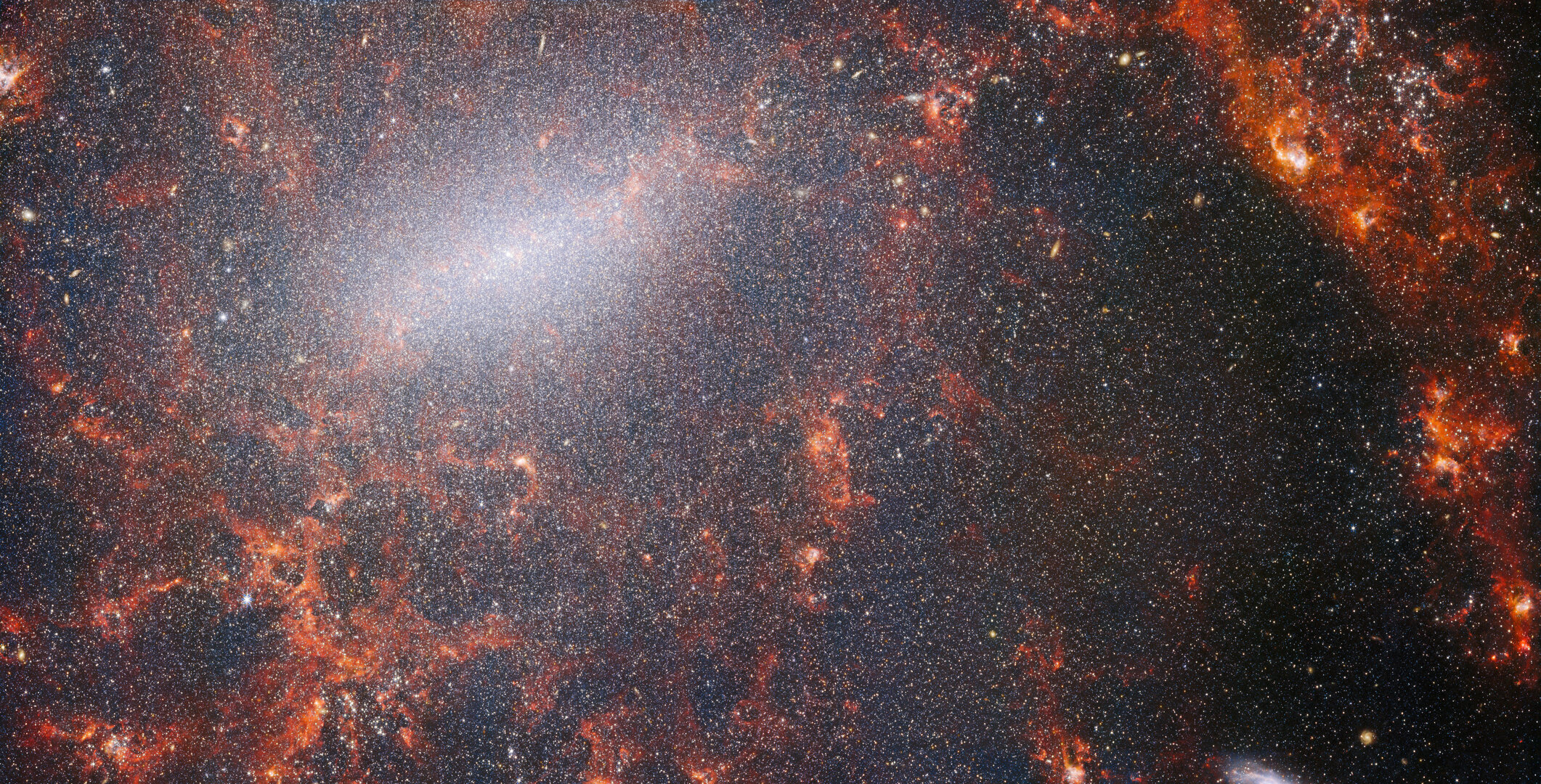 A delicate tracery of dust and bright star clusters threads across this image from the NASA/ESA/CSA James Webb Space Telescope. This view from Webbâs NIRCam instrument is studded by the galaxyâs massive population of stars, most dense along its bright central bar, along with burning red clouds of gas illuminated by young stars within. These glittering stars belong to the barred spiral galaxy NGC 5068, located around 17 million light-years from Earth in the constellation Virgo. This portrait of NGC 5068 is part of a campaign to create an astronomical treasure trove, a repository of observations of star formation in nearby galaxies. Previous gems from this collection can be seen here and here. These observations are particularly valuable to astronomers for two reasons. The first is because star formation underpins so many fields in astronomy, from the physics of the tenuous plasma that lies between stars to the evolution of entire galaxies. By observing the formation of stars in nearby galaxies, astronomers hope to kick-start major scientific advances with some of the first available data from Webb. The second reason is that Webbâs observations build on other studies using telescopes including the NASA/ESA Hubble Space Telescope and some of the worldâs most capable ground-based observatories. Webb collected images of 19 nearby star-forming galaxies which astronomers could then combine with catalogues from Hubble of 10 000 star clusters, spectroscopic mapping of 20Â 000 star-forming emission nebulae from the Very Large Telescope (VLT), and observations of 12Â 000 dark, dense molecular clouds identified by the Atacama Large Millimeter/submillimeter Array (ALMA). These observations span the electromagnetic spectrum and give astronomers an unprecedented opportunity to piece together the minutiae of star formation. This near-infrared image of the galaxy is filled by the enormous gathering of older stars which make up the core of NGC 5068. The keen vision of NIRCam allows astronomers to peer through the galaxyâs gas and dust to closely examine its stars. Dense and bright clouds of dust lie along the path of the spiral arms: these are H II regions, collections of hydrogen gas where new stars are forming. The young, energetic stars ionise the hydrogen around them which, when combined with hot dust emission, creates this reddish glow. H II regions form a fascinating target for astronomers, and Webbâs instruments are the perfect tools to examine them, resulting in this image. [Image Description: A close-in image of a spiral galaxy, showing its core and part of a spiral arm. At this distance thousands upon thousands of tiny stars that make up the galaxy can be seen. The stars are most dense in a whitish bar that forms the core, and less dense out from that towards the arm. Bright red gas clouds follow the twist of the galaxy and the spiral arm.] Links  NGC 5068 (NIRCam+MIRI Image) NGC 5068 (MIRI Image) Slider Tool (MIRI and NIRCam images) Video: Pan of NGC 5068 Video: Webb's views of NGC 5068 (MIRI and NIRCam images) Video: Zoom into NGC 5068 