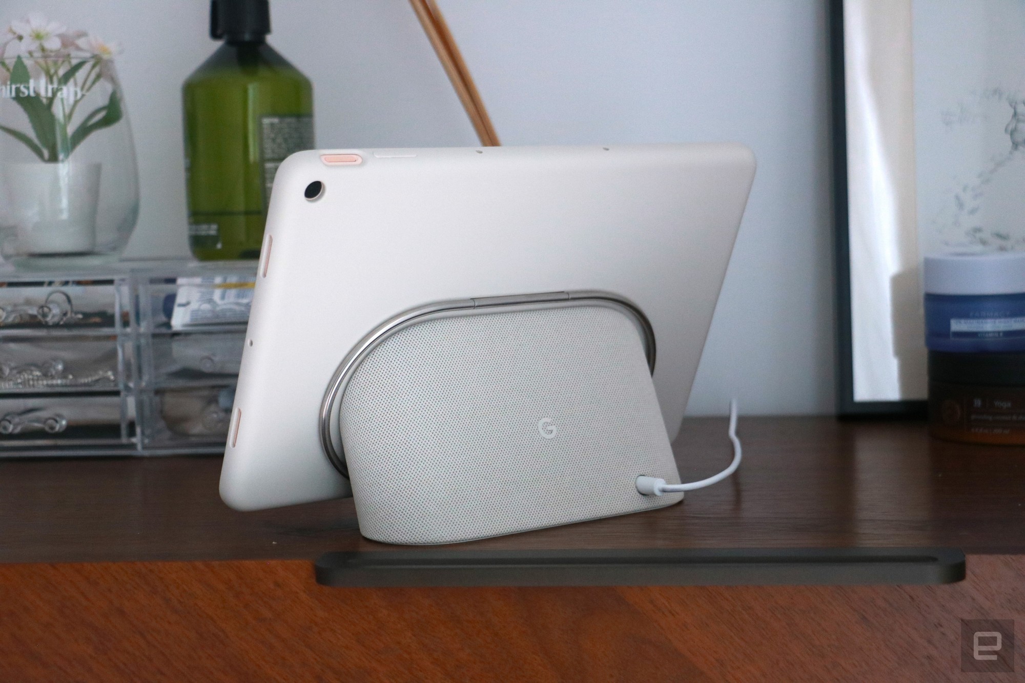 The Pixel Tablet with its protective case on and docked on the speaker base. Its silver kickstand, which is folded in, is a ring that circles the speaker.