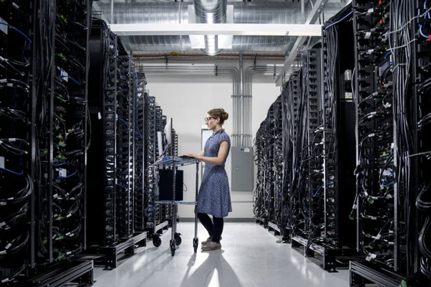 Eine Person steht mit einem Computerterminal inmitten einer Serverfarm.