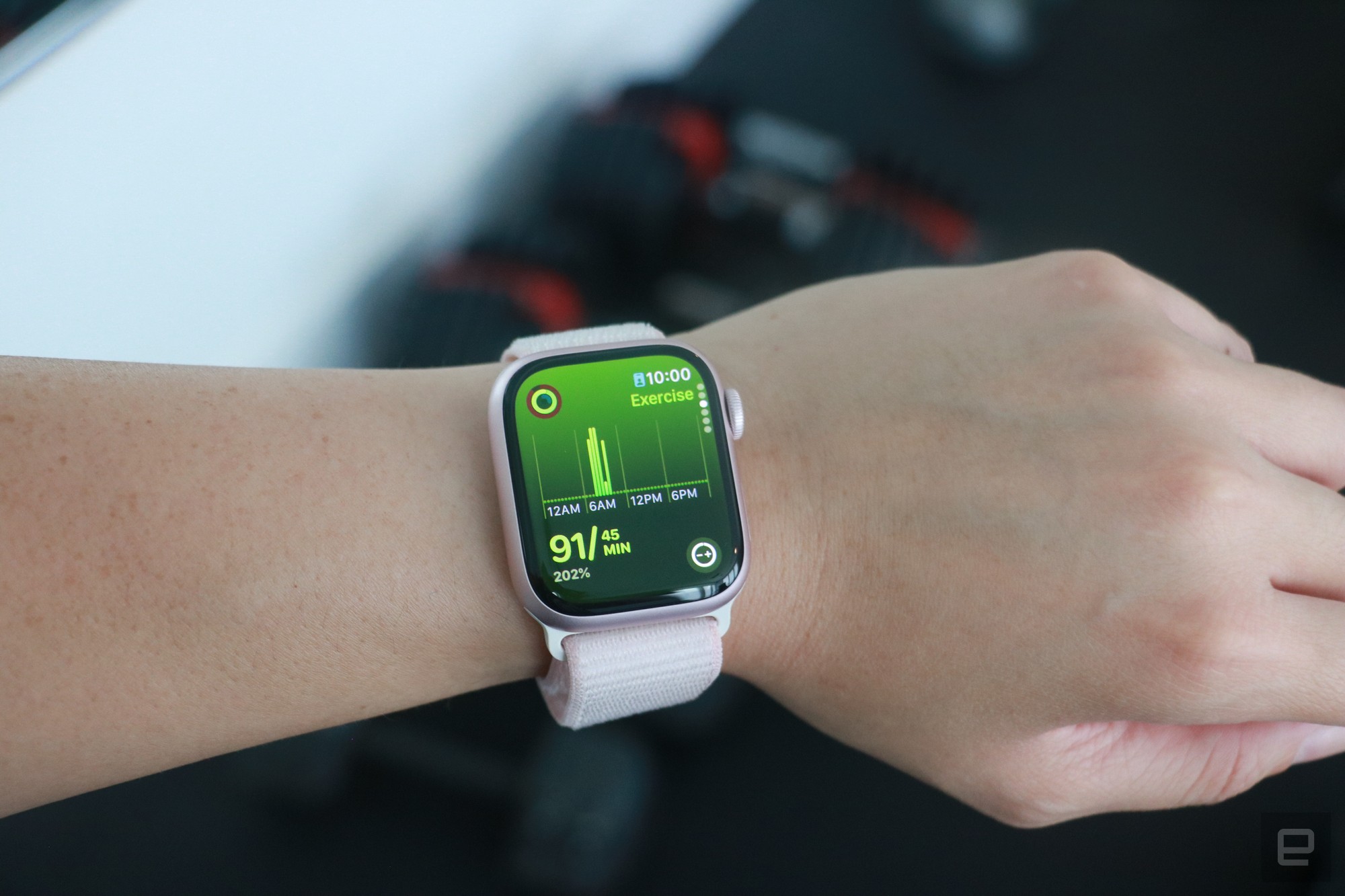 The Apple Watch Series 9 on a person's wrist in front of some gym equipment, showing the Exercise page of the Move rings app.