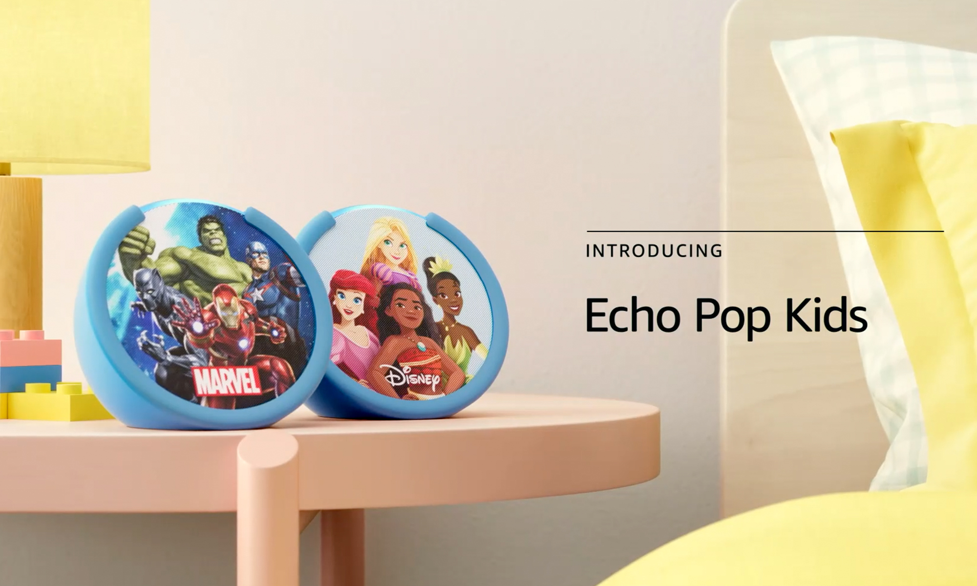 Product photo for Amazon Echo Pop Kids. A Marvel-themed speaker sits next to a Disney Princess speaker on a child's bedside table.