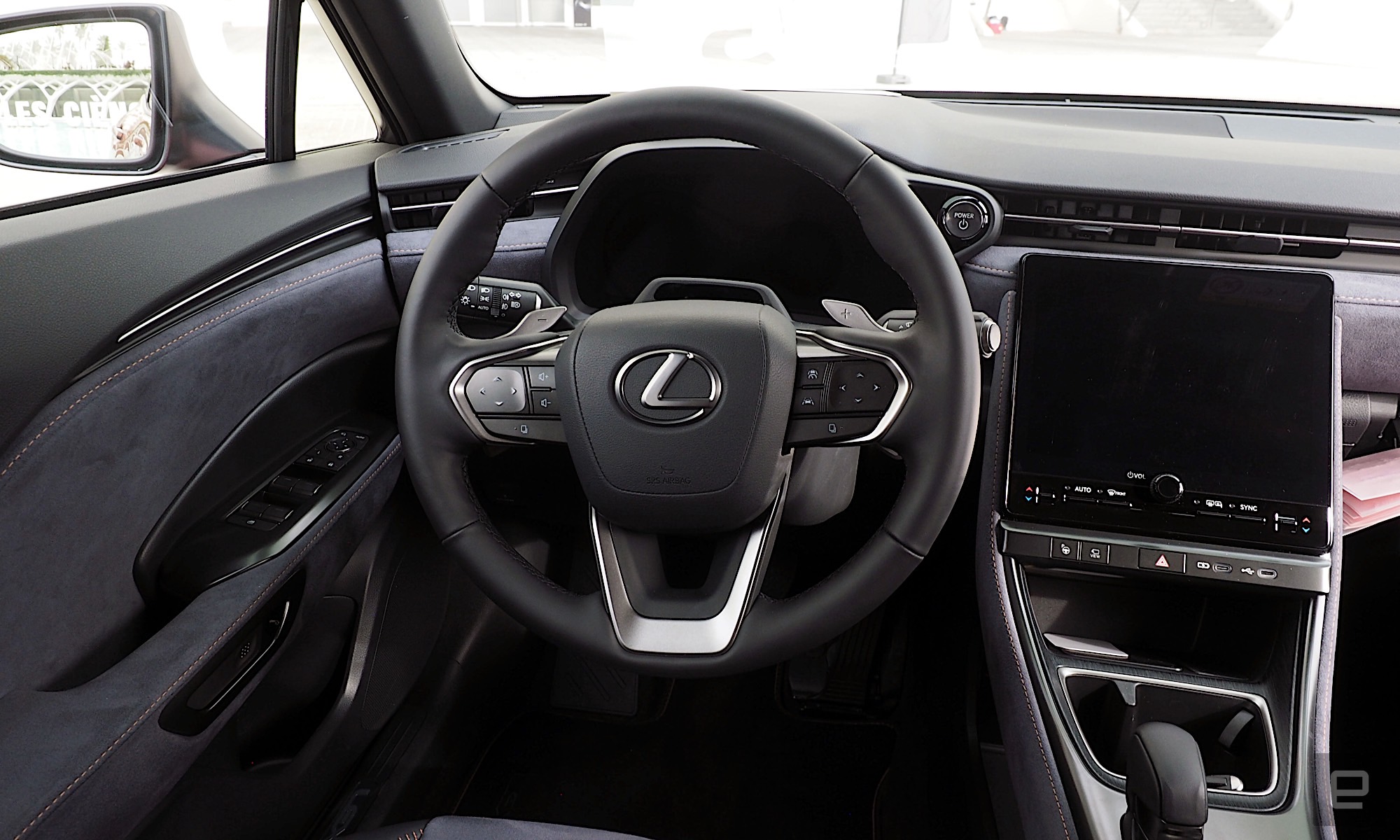 Image of the driver position inside a Lexus LBX with a dark grey and black interior, the wheel stands in front of a digital instrument binnacle while an infotainment system sits to its right.