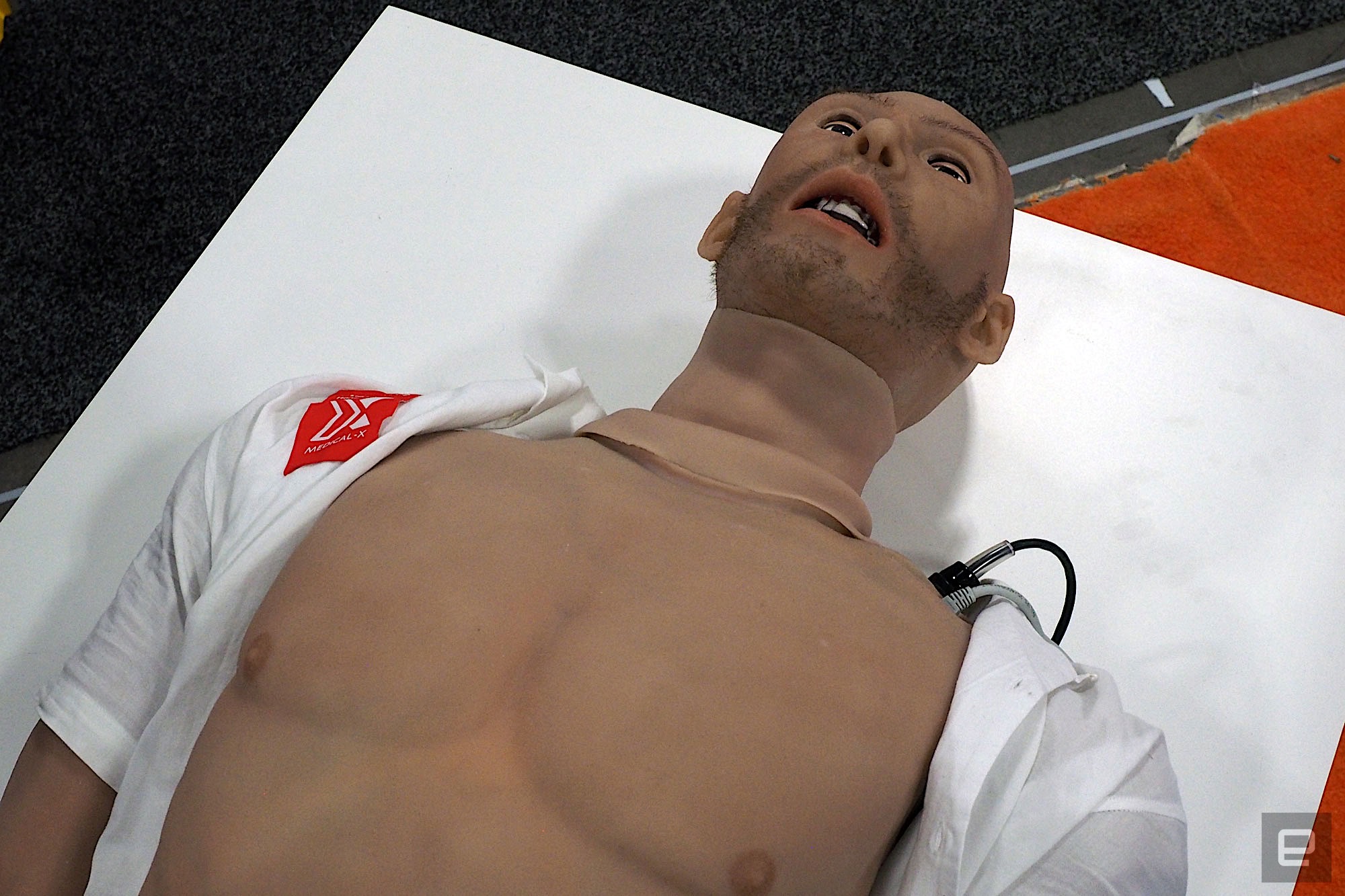 An image of the Adam-X medical training robot, an artificial human body lying on a white podium with its shirt open.