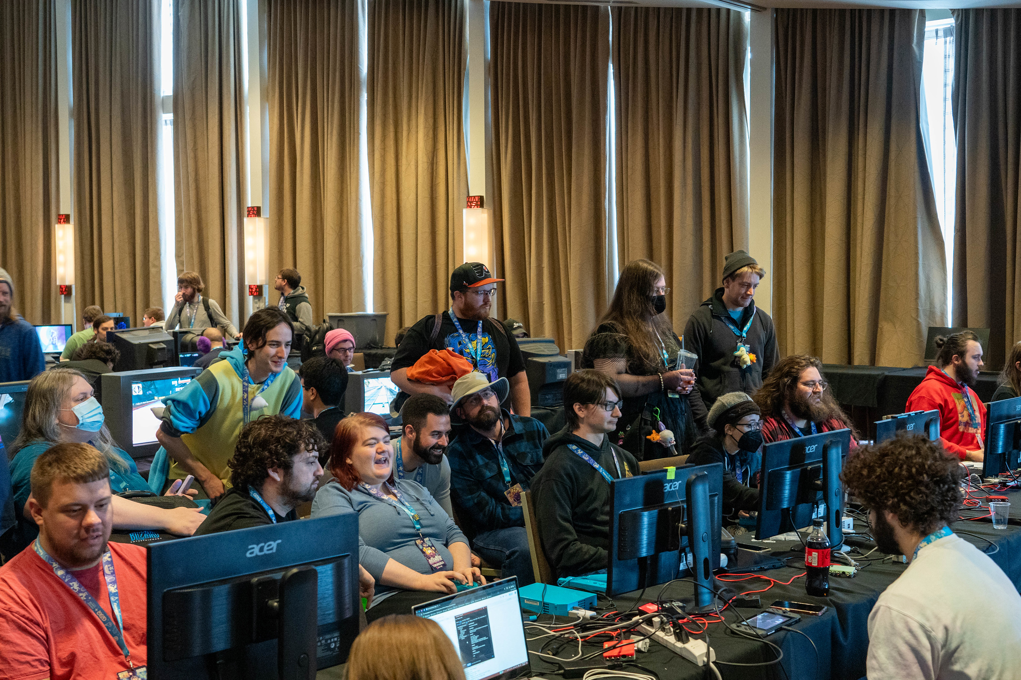 A conference room full of gamers and speedrunners playing and watching games on various computer monitors.