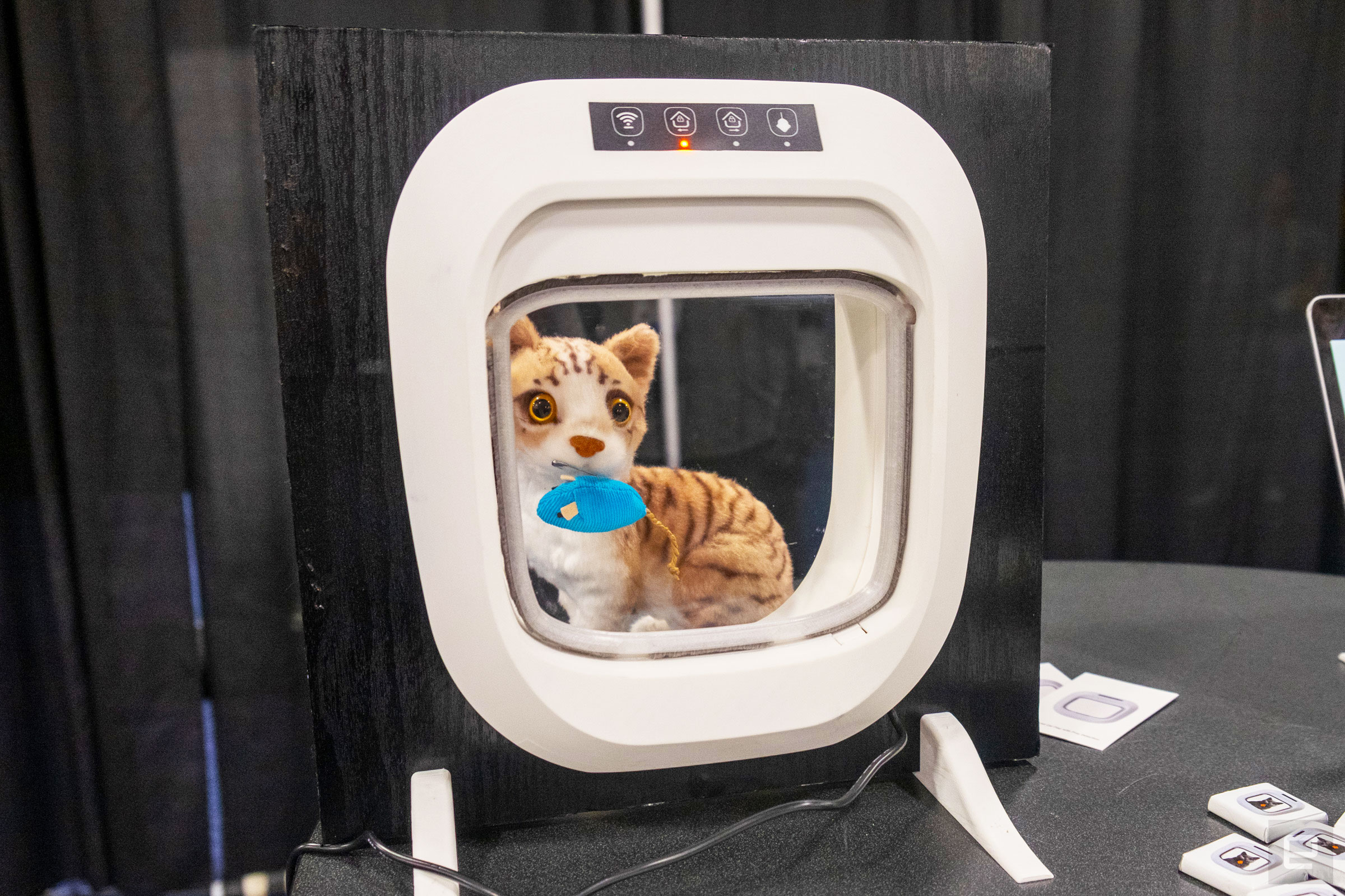 A white Flappie cat door installed in a square of black wood with a stuffed cat and mouse behind it on display at CES 2024.