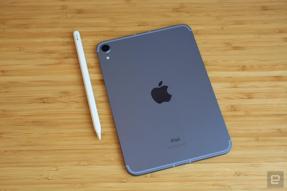 Photo of the 6th-generation iPad mini sitting on a sleek wooden table with its back (with Apple logo) facing up. Its Apple Pencil sits to its left.