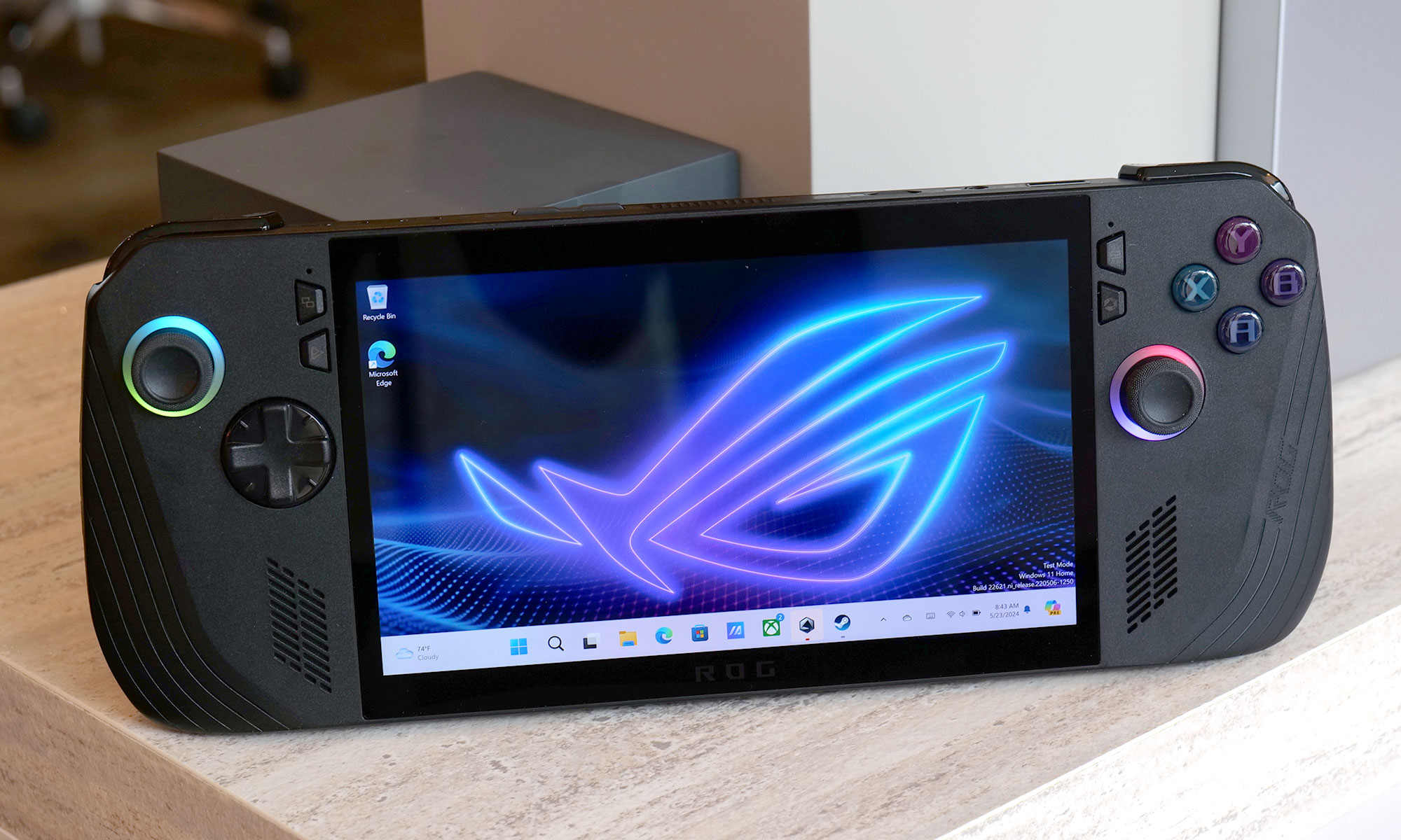 The ASUS ROG Ally X gaming handheld leaning against some cubic ornaments, with the Windows home page on its screen.