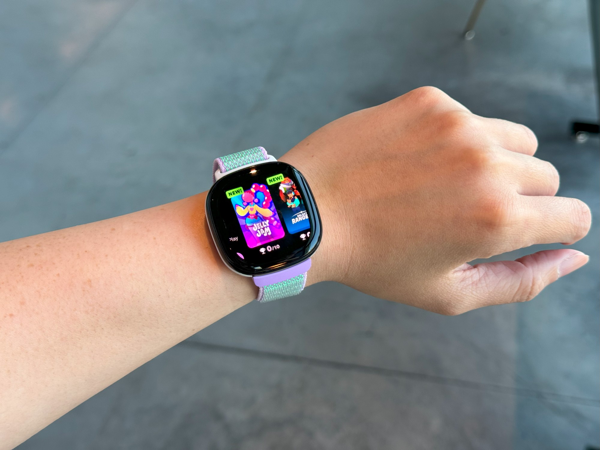 The Fitbit Ace LTE on a wrist held in mid-air, with two game titles on a carousel in view: 