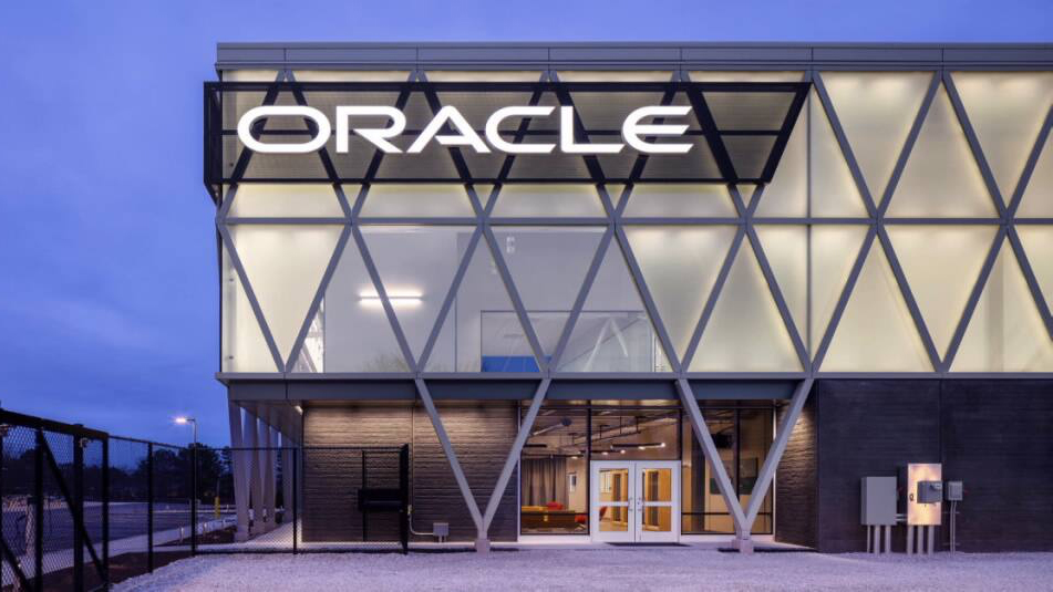 A building at Oracle headquarters with the company's logo. Dusky blue sky.