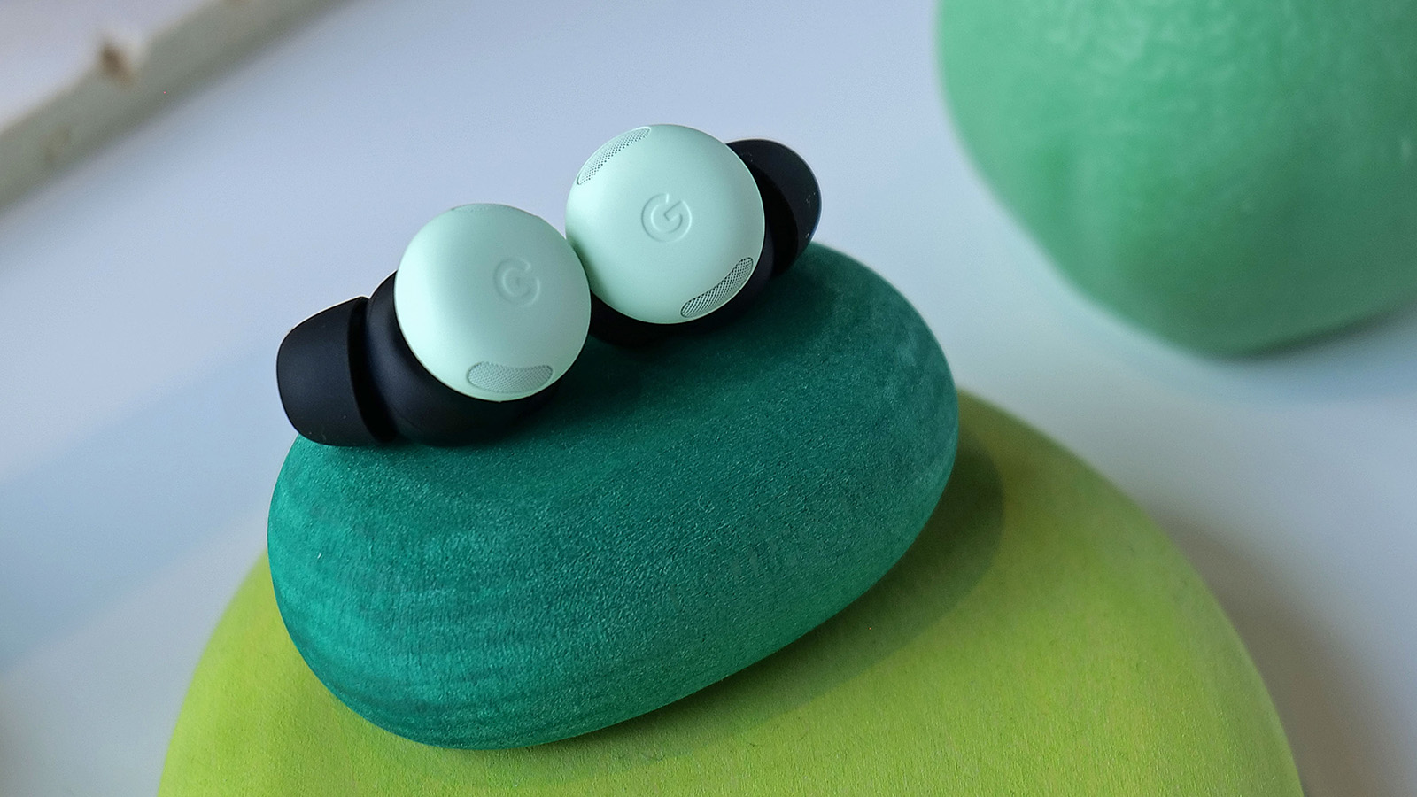 A closeup of the Pixel Buds Pro 2 in Wintergreen sit on a green rock. 