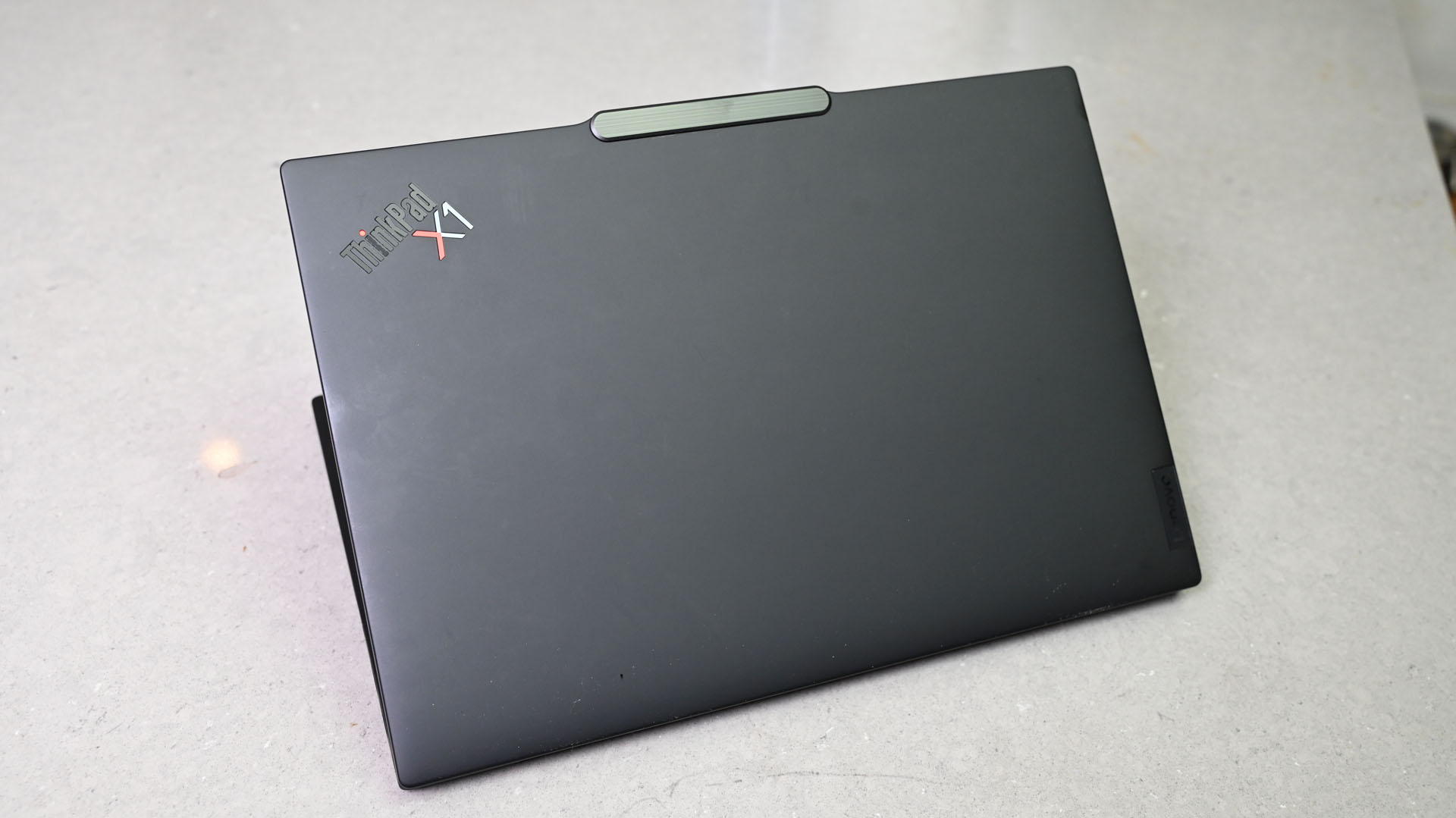 The Lenovo ThinkPad X1 Carbon (12th-gen) slightly folded and on a marble counter with its lid facing out.