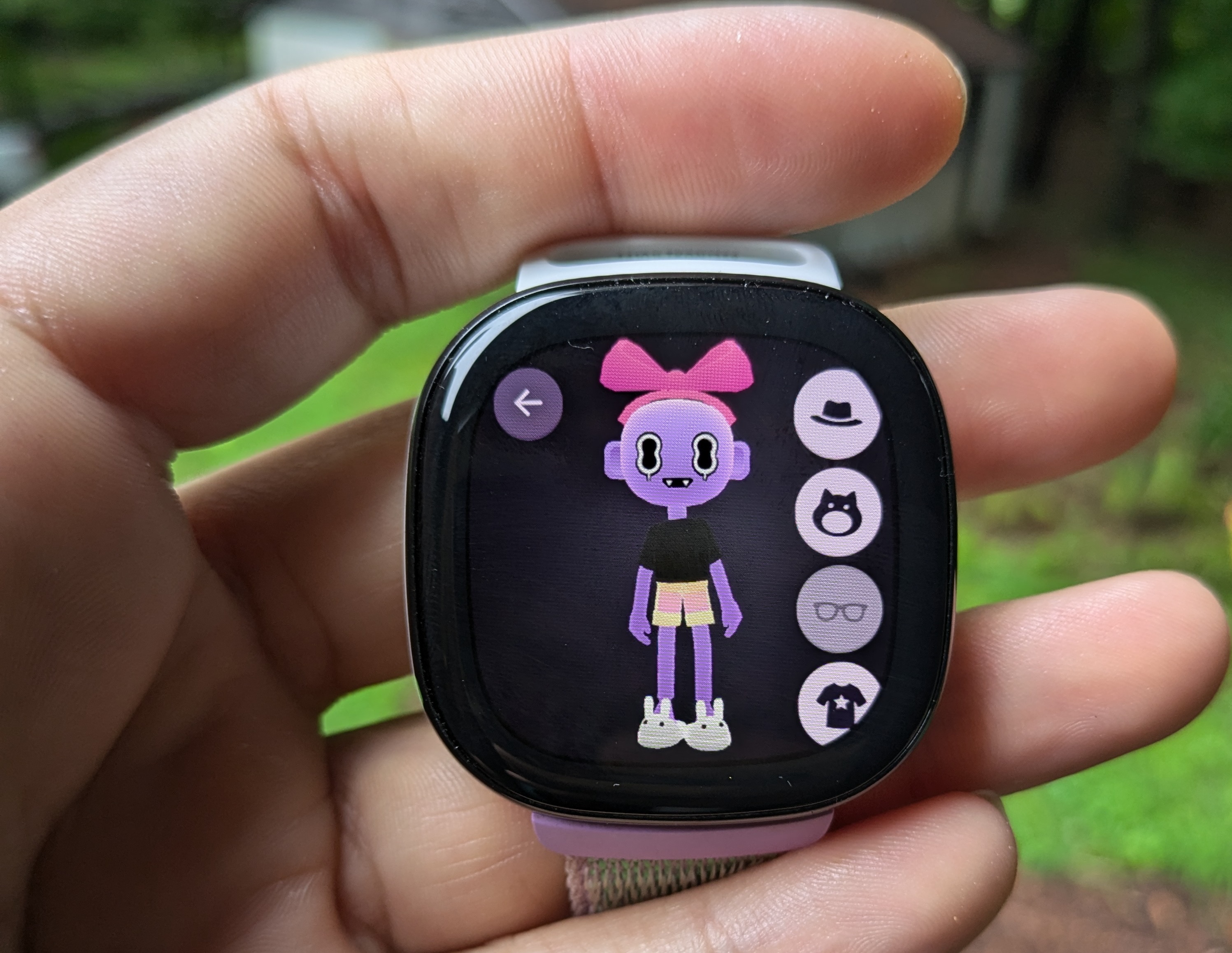 A Fitbit Ace LTE showing the eejie character builder. An eejie (humanoid virtual companion) is pictured. It has purple skin, big eyes, and fangs, and is wearing a pink bow on its head, light orange shorts and white bunny slippers