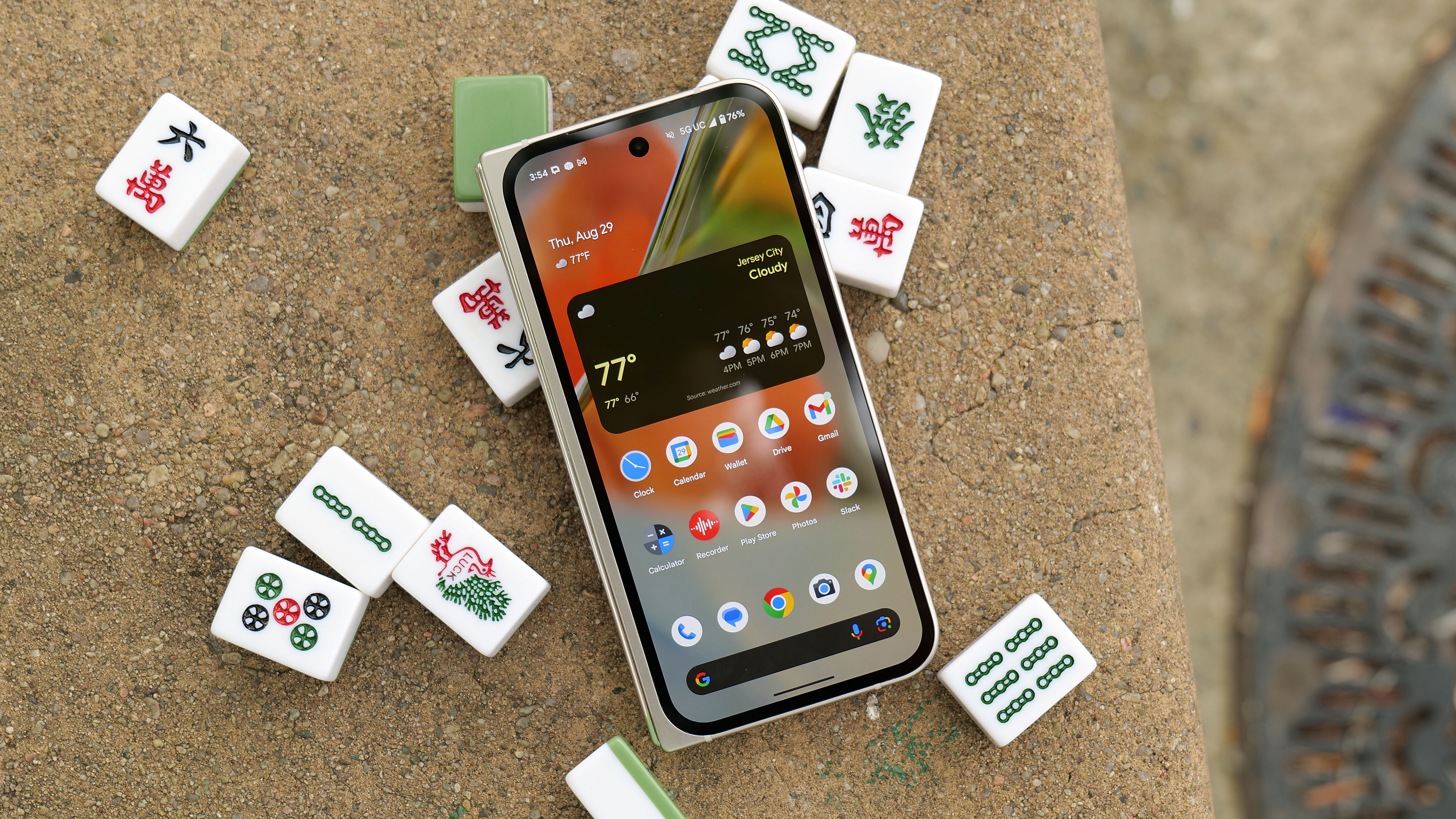 The Pixel 9 Pro Fold, closed, with its external display facing up, on top of a bunch of mahjong tiles on a park table.