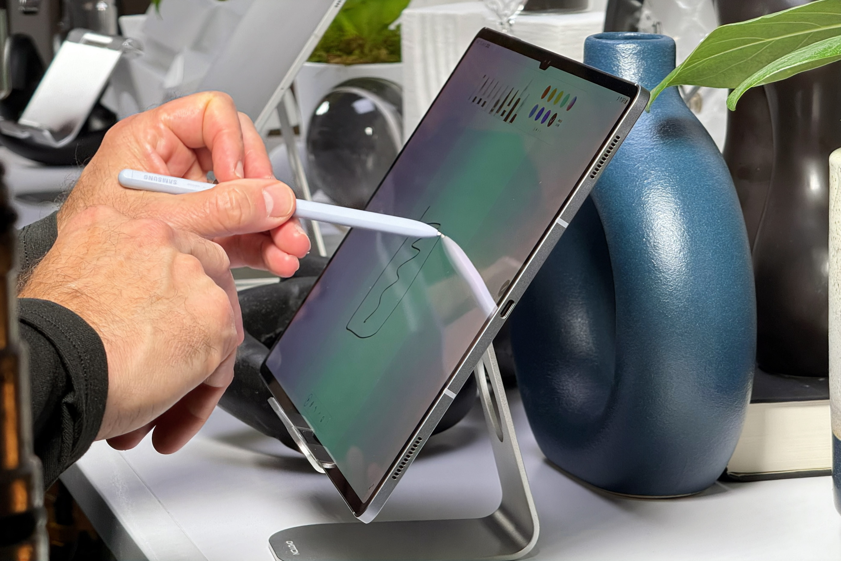 Side view of a Galaxy Tab S10 Ultra on a stand with a hand holding an S Pen and drawing on it.