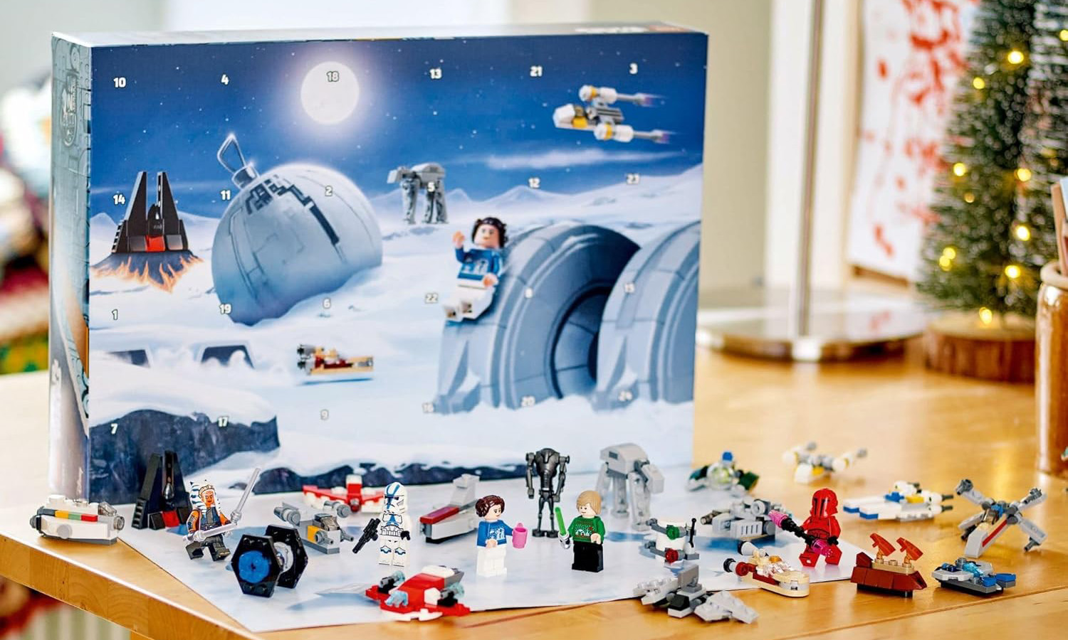 The Lego Star Wars advent calendar is arranged on a table with a xmas tree in the background. 