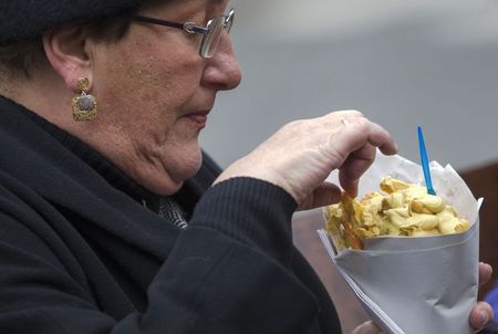 A woman eats fries with mayonnaise sauce on a bench near the Maison Antoine frites stand - 2014-12-05T132244Z_1_LYNXNPEAB40N4_RTROPTP_2_BELGIUM-FRIES