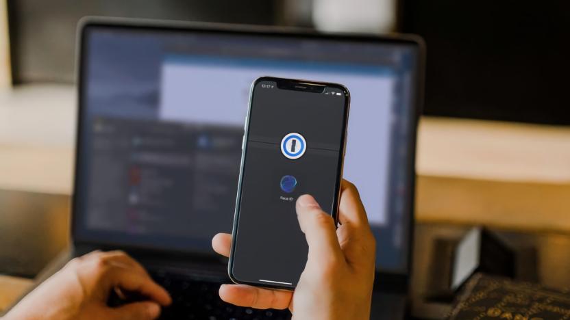 A person holding an iPhone with the 1Password app open. A laptop is in the background.