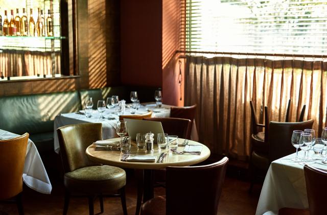 Empty restaurant prepared for evening meal with computer on table and place settings