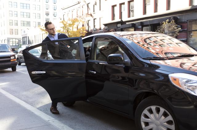 Young man, businessman getting into the back of a black car on a beautiful sunny day, door is open as he gets into the car with his briefcase, Commuting to work or going to the airport