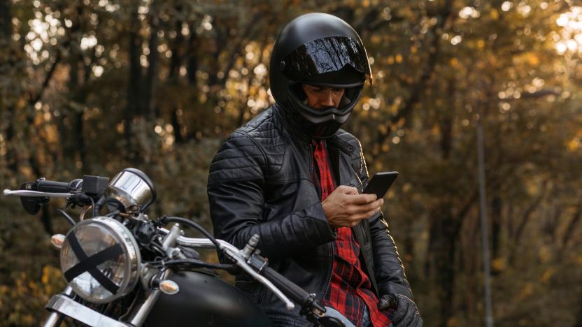 Caucasian male biker sitting on his motorbike and using his smart phone