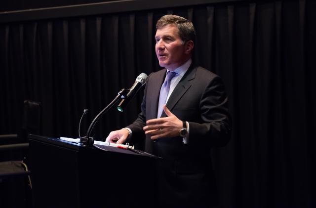 A man in a suit standing behind a podium with a mic.