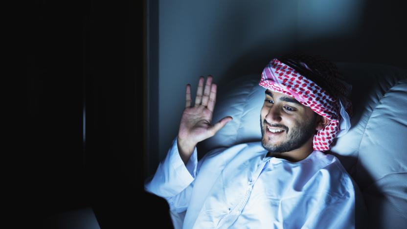 Waving to his family from overseas, a young middle eastern man connects with his family via video conferencing late at night thanks to a digital tablet.