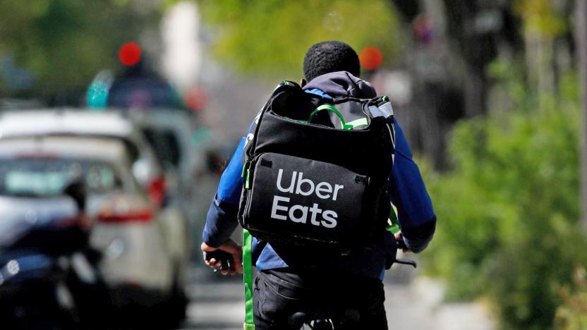 An Uber Eats delivery person rides down a path with their logo-emblazoned delivery backpack.