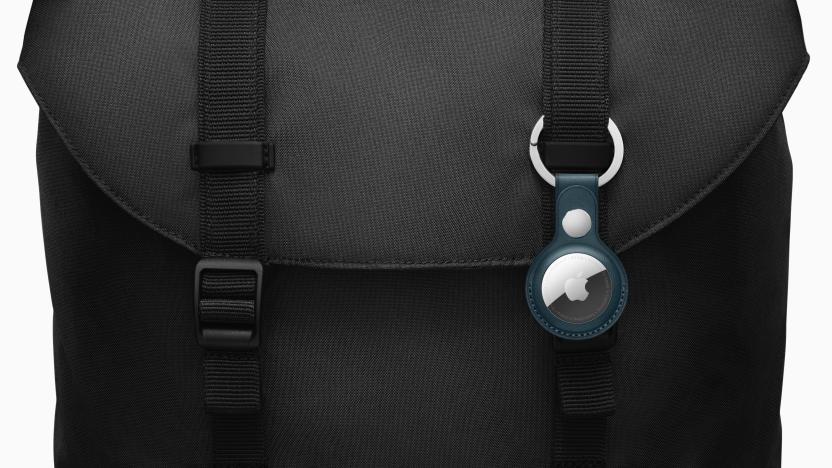 An Apple AirTag in a navy blue case clipped to the outside of a black backpack