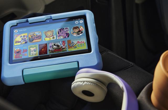 Amazon Fire 7 Kids tablet in a blue case on a car seat next to a set of headphones and a cup.