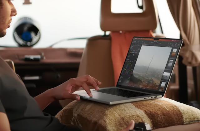 A man in a backseat of a van, working on a project on a new MacBook Pro