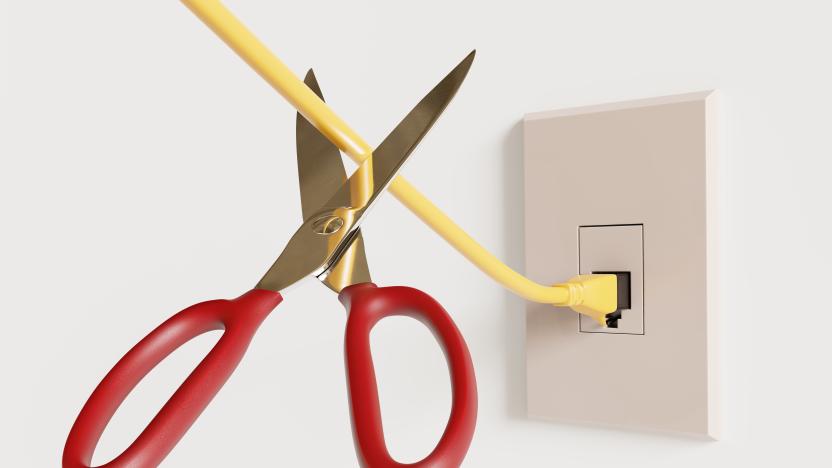 A pair or red scissors about to snip an ethernet cable connected to the wall