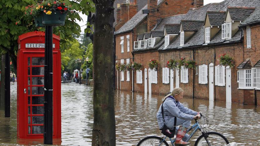 A woman rides a bicycle through a foot of water next to an iconic British red telephone box.