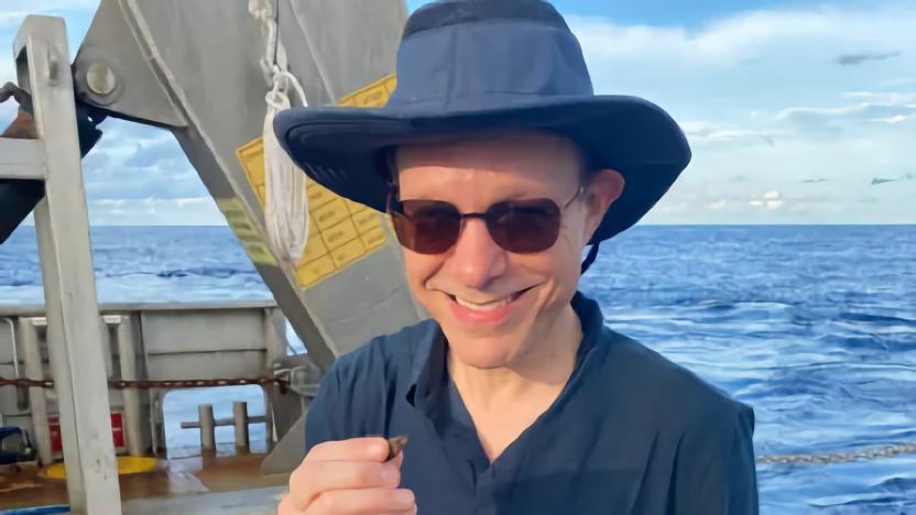 Photo of Harvard astrophysicist, on a boat with sunglasses and hat, holding a small object in his hand.
