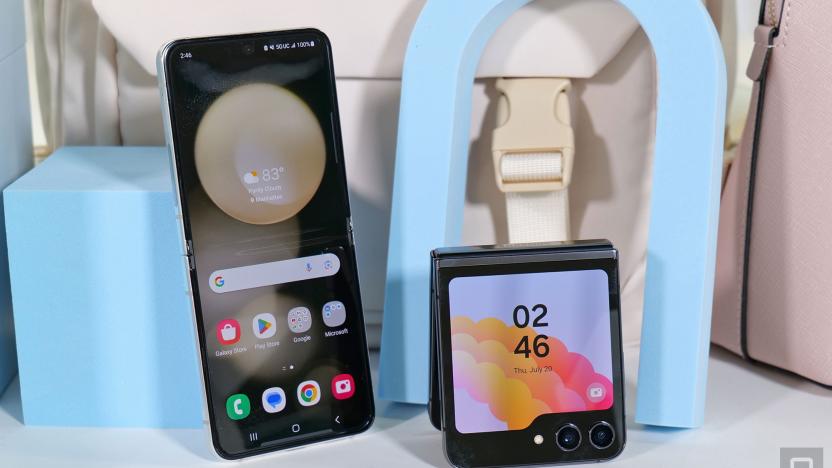 A Galaxy Z Flip 5 leaning against a pastel blue cube with its inside screen facing the camera, next to another Galaxy Z Flip 5 folded in half and propped up with its outside display facing the camera.