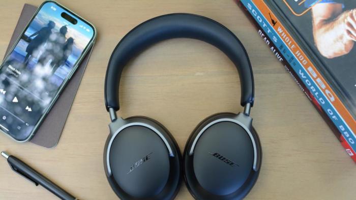 Review photo of the Bose QuietComfort Ultra headphones, sitting on a table next to a pen, phone and books.