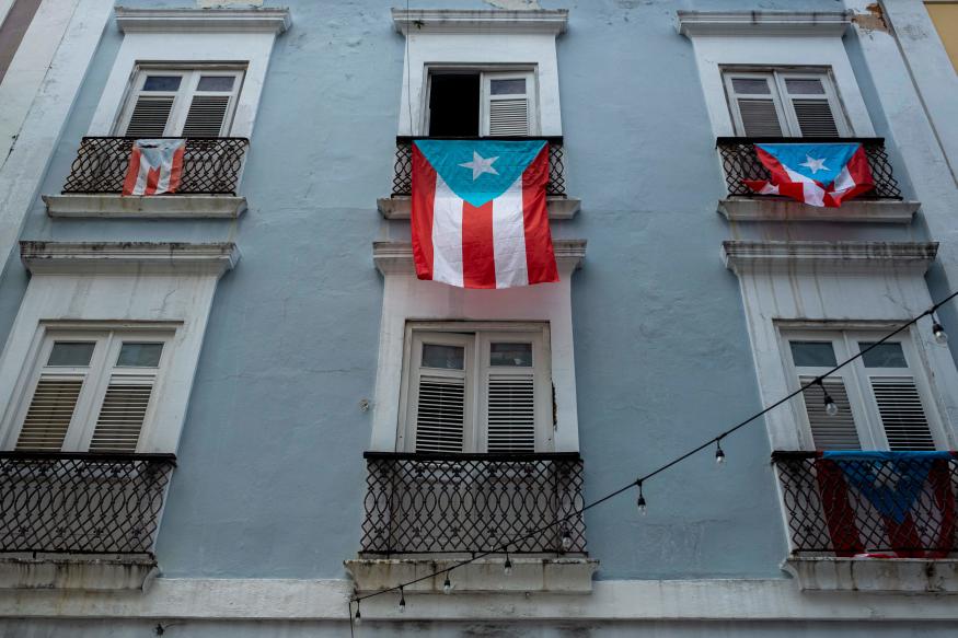 Puerto Rican National flags hang from balconies in Old San Juan, Puerto Rico on April 7, 2020. - On March 15, 2020, Puerto Rico Governor Wanda Vazquez Garced imposed a curfew shuttering non-essential businesses on the island and ordered people to stay home from 7 p.m. to 5 a.m. In addition, from March 31, she imposed even tighter measures, including requiring anyone entering a business to wear a face mask. (Photo by Ricardo ARDUENGO / AFP) (Photo by RICARDO ARDUENGO/AFP via Getty Images)