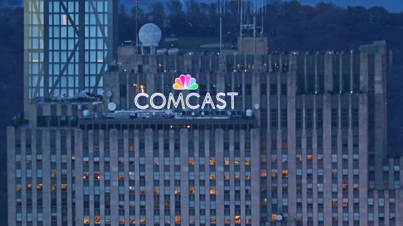 A comcast and NBC peacock sign on top of an office building photographed from a distance.