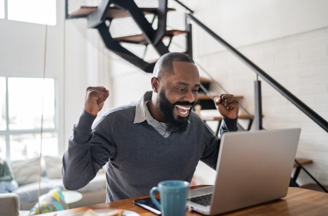 Happy man celebrating good news using laptop at home