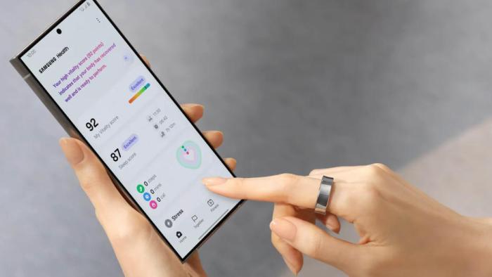 Galaxy Ring lifestyle image, showing a person wearing the ring on their left index finger while navigating the Samsung Health app on a Galaxy smartphone.