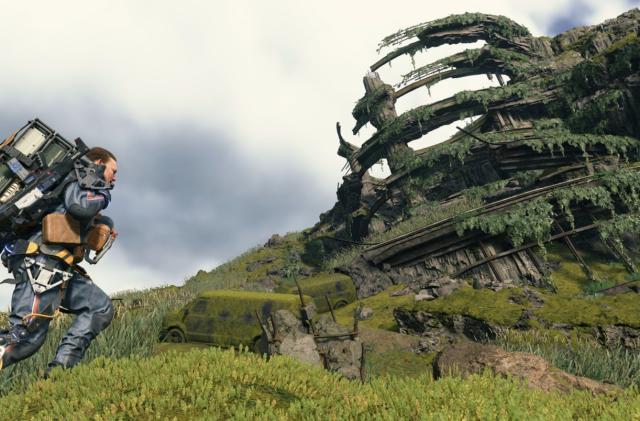 A male character bearing an overladen backpack climbs a grassy hill. A decaying circular structure is in the background.