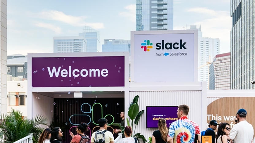 A Slack setup at an outdoor event. Signs say "Welcome" next to the "Slack from Salesforce" logo. People mill about.