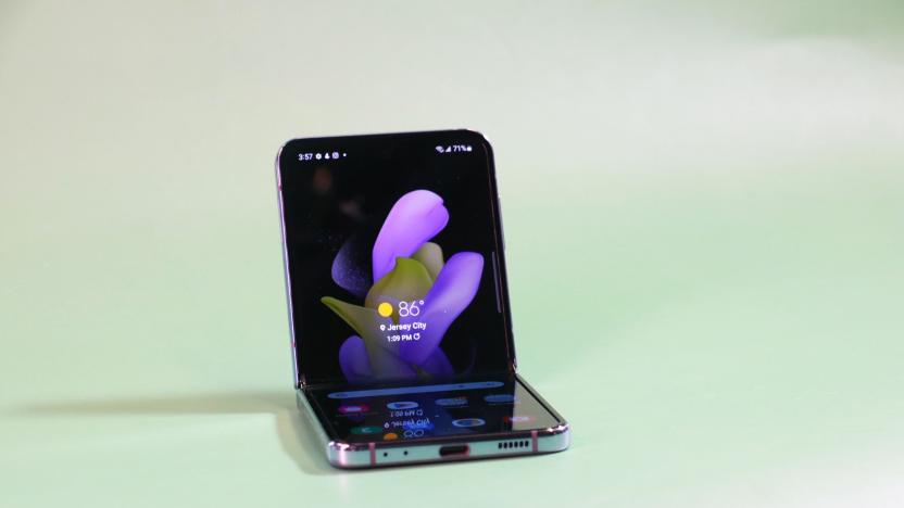 The Galaxy Z Flip 4 half folded and sitting up on a green surface with its screen facing out.