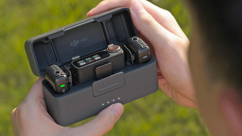 An over-the-shoulder view of DJI's updated Mic 2 in its charging case being opened by someone with blurred grass in the background.