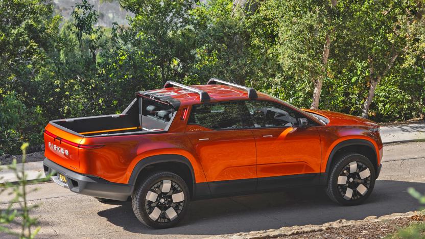 A Fisker Alaska 2023 pickup in burnt orange color is seen driving along a wooded road on a hillside, with trees flanking the road.