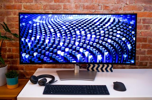 Dell's UltraSharp 40 Curved Thunderbolt Hub Monitor on a desk with a keyboard, mouse and headphones placed in front.