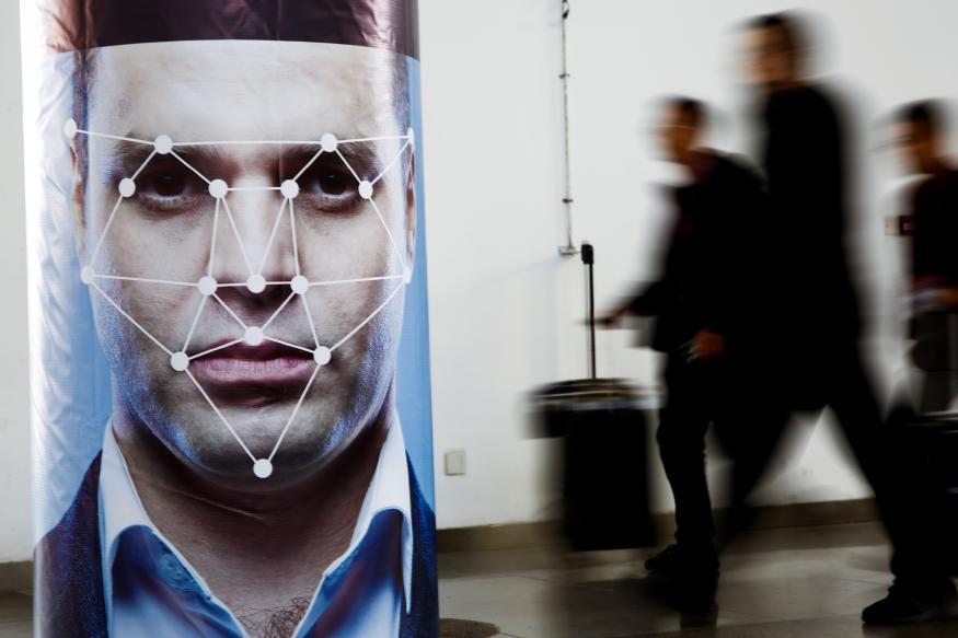 People walk past a poster simulating facial recognition software at the Security China 2018 exhibition on public safety and security in Beijing, China October 24, 2018.   REUTERS/Thomas Peter