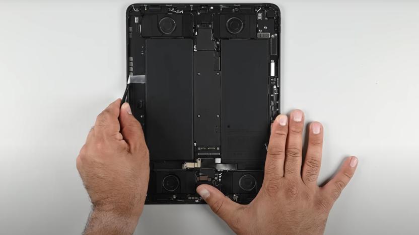 The new iPad Pro with the screen removed, a person's hands are seen holding it and using a tool to access pull tabs beneath one of the battery cells