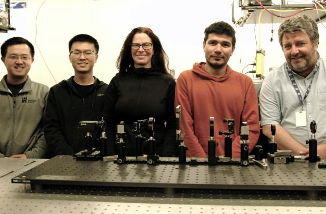 Group photo of five members of a research team focused on a scientific camera. They stand smiling in a laboratory with various imagine equipment on the research table in front of them.