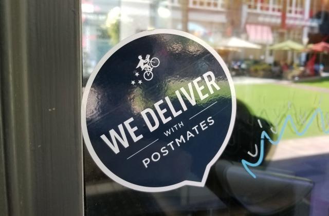 Close-up of logo reading We Deliver With Postmates, referencing the Postmates food delivery app service, on a restaurant window in the Silicon Valley, San Jose, California, June 7, 2018. (Photo by Smith Collection/Gado/Getty Images)