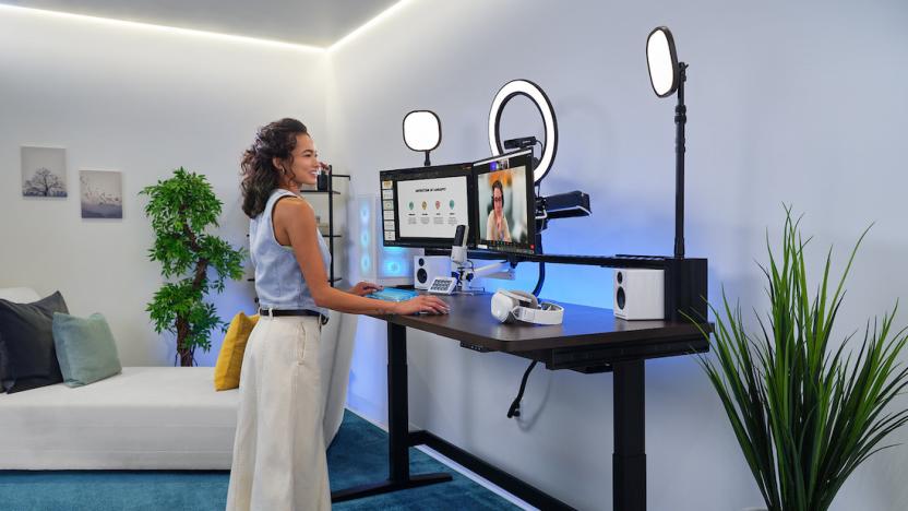 A woman works at a standing desk with two monitors facing her. 